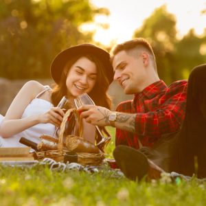 Clinking glasses with wine. Caucasian young couple enjoying weekend in the park on summer day. Look lovely, happy, cheerful. Concept of love, relationship, wellness, lifestyle. Sincere emotions.